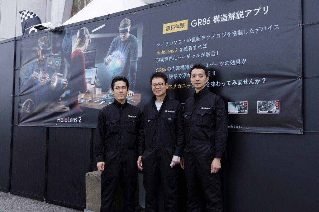 ブース展示「GR86 構造解説アプリ」前に並ぶ作業着を着た3名の男性