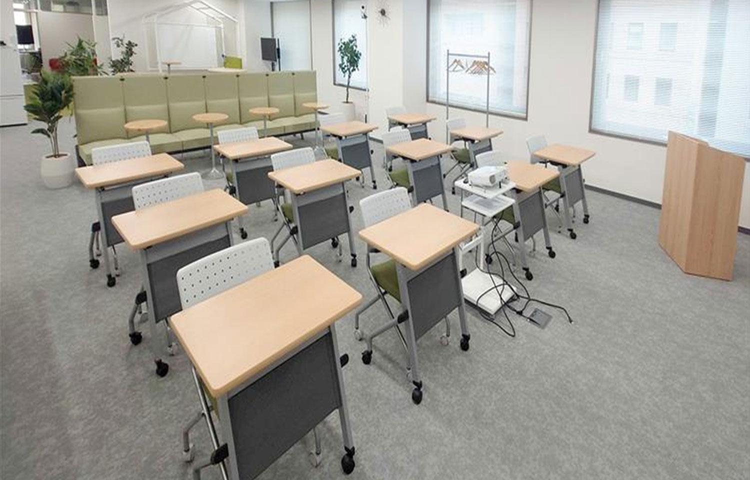 キャスター付きの個別机がプロジェクターに向かって並び、奥にグリーンのベンチ席がある可変型教室。