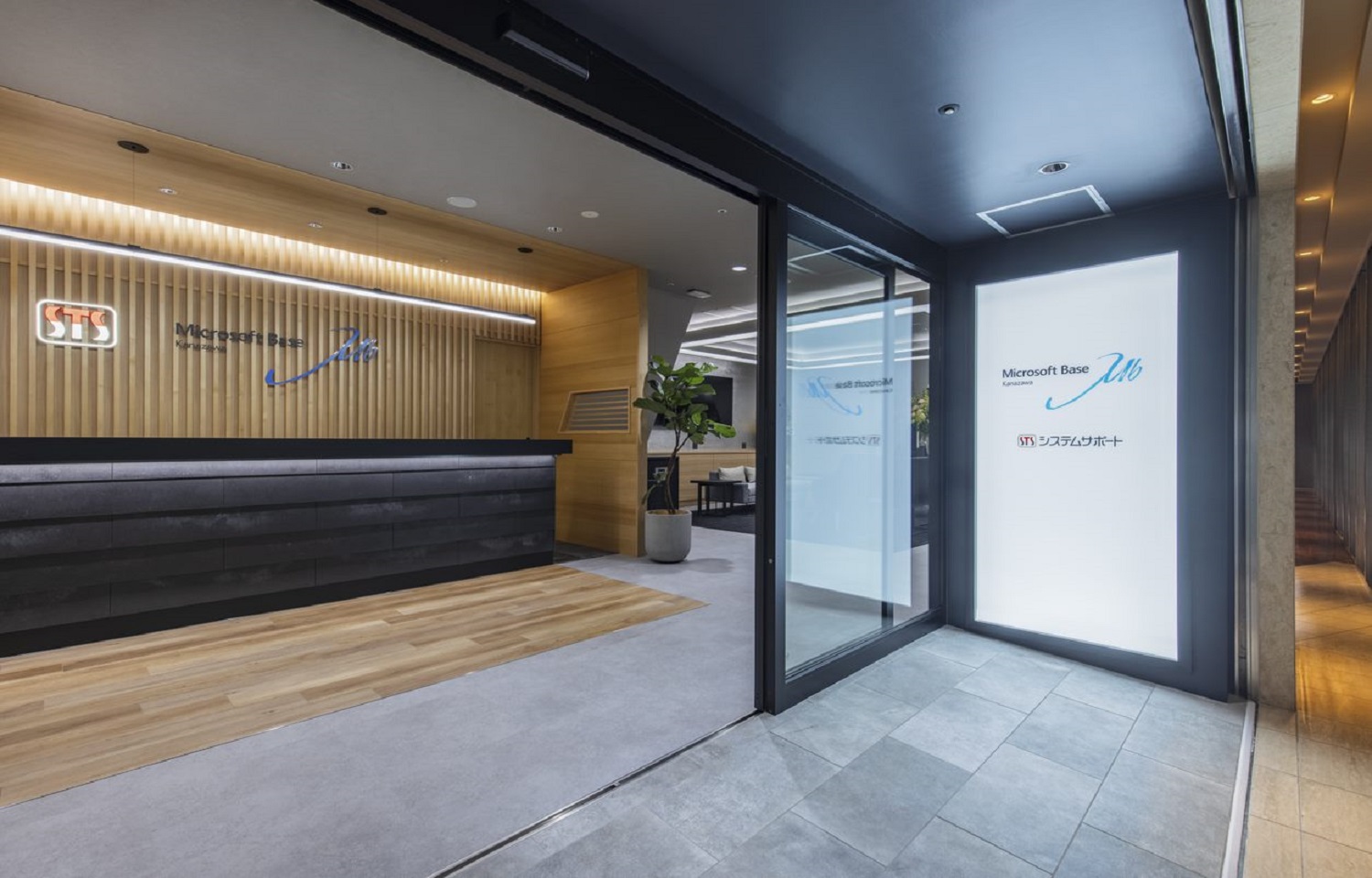 木製ルーバーの壁と受付カウンター、ガラス扉に「Microsoft Base」と表示されたエントランス。