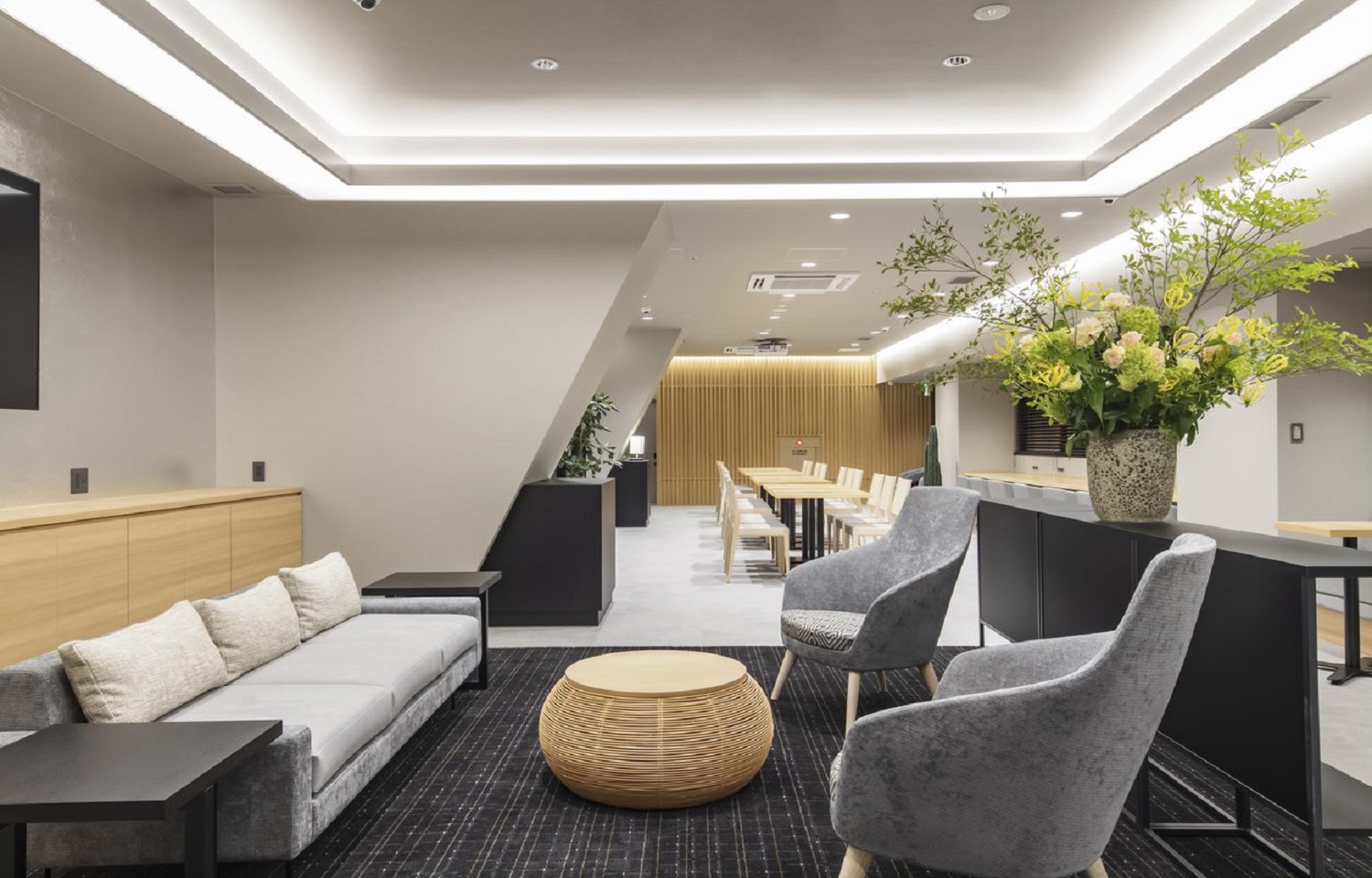 ソファとアームチェア、編みのローテーブルがある落ち着いたラウンジ。奥に長いダイニングエリア。