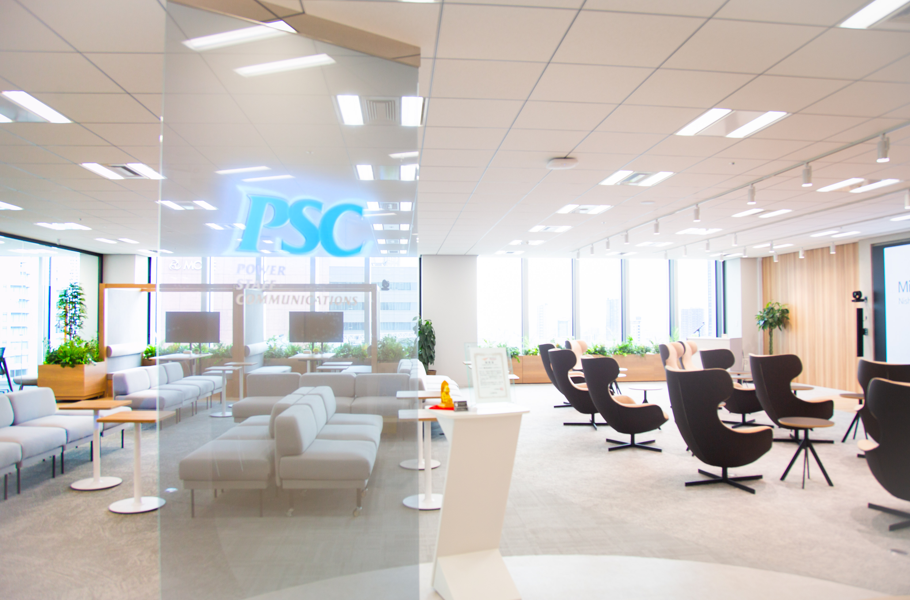 明るい開放的なラウンジ、モジュールソファと回転式アームチェア、ガラス仕切りにPSCの表示。