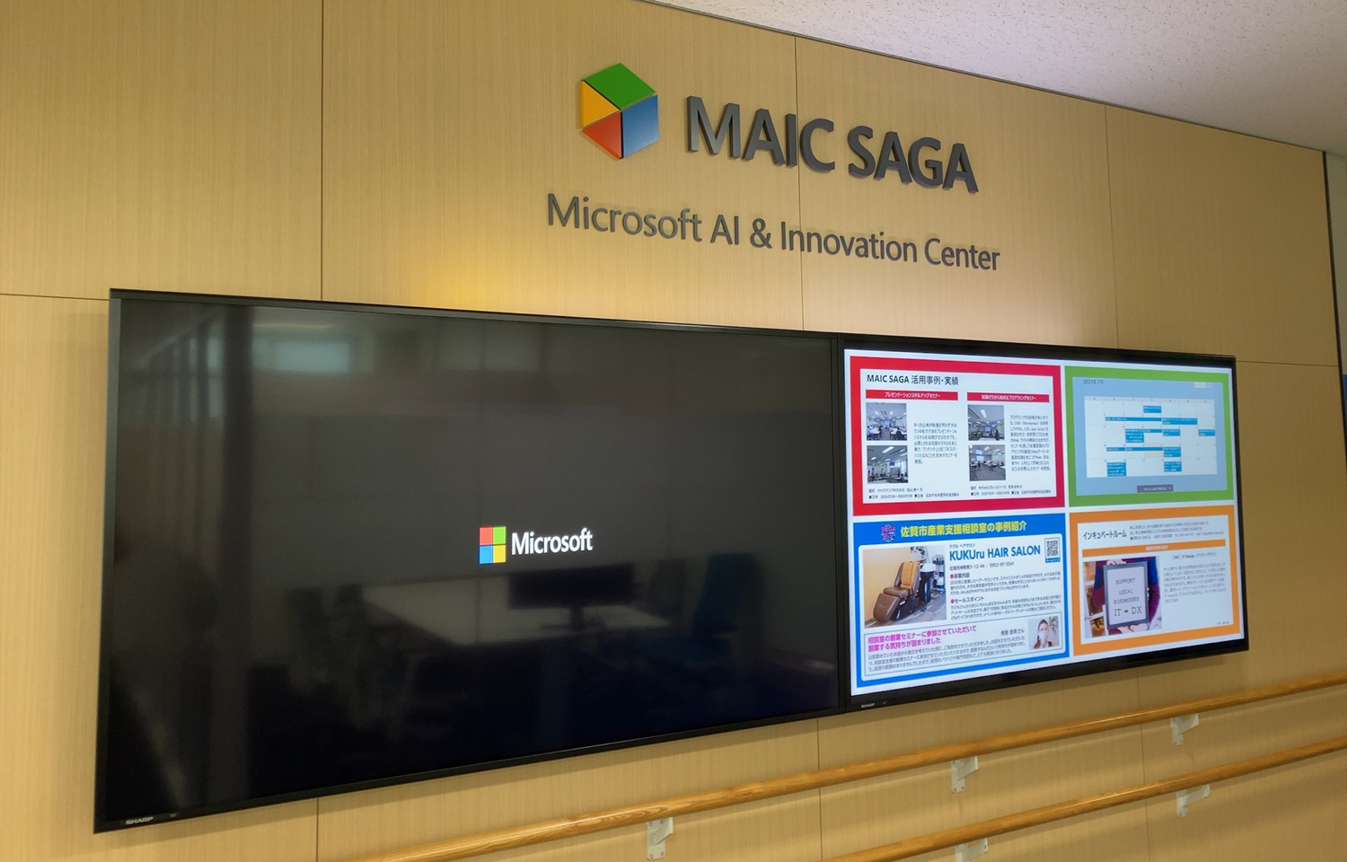「MAIC SAGA - Microsoft AI & Innovation Center」の看板が掲げられた室内の壁に、Microsoftロゴを表示した大型スクリーンと「KUKUru HAIR SALON」などの情報コンテンツを映すスクリーンが設置されています。