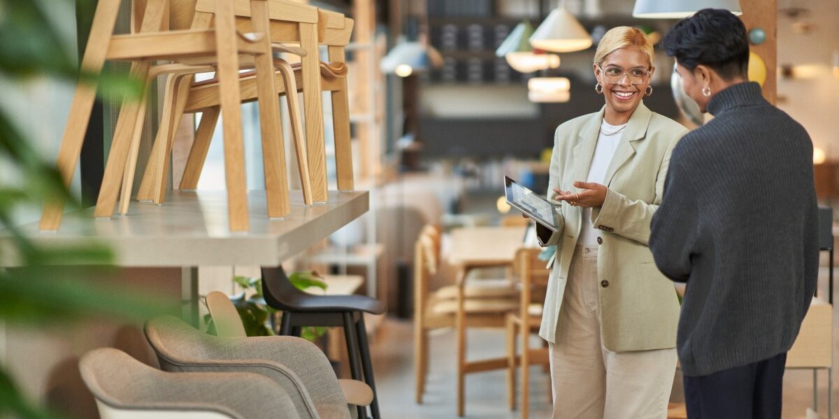 Retail store manager working with a customer, showing merchandise and providing customer service on-the-go using a tablet to locate inventory and place orders.