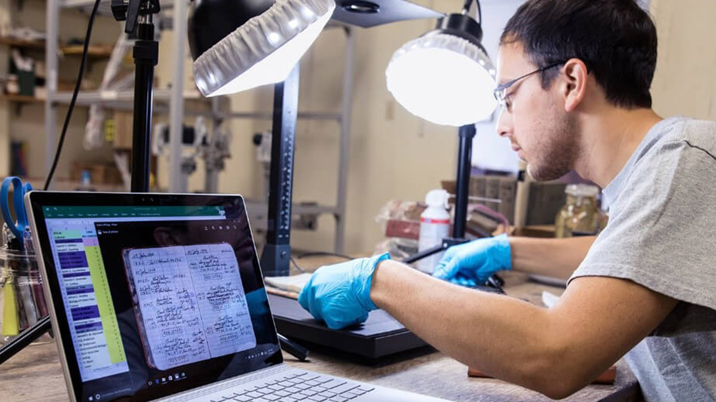 Mannelijke jongvolwassene zit in een lab waar hij een onderzoeksresultaat op een laptop verwerkt