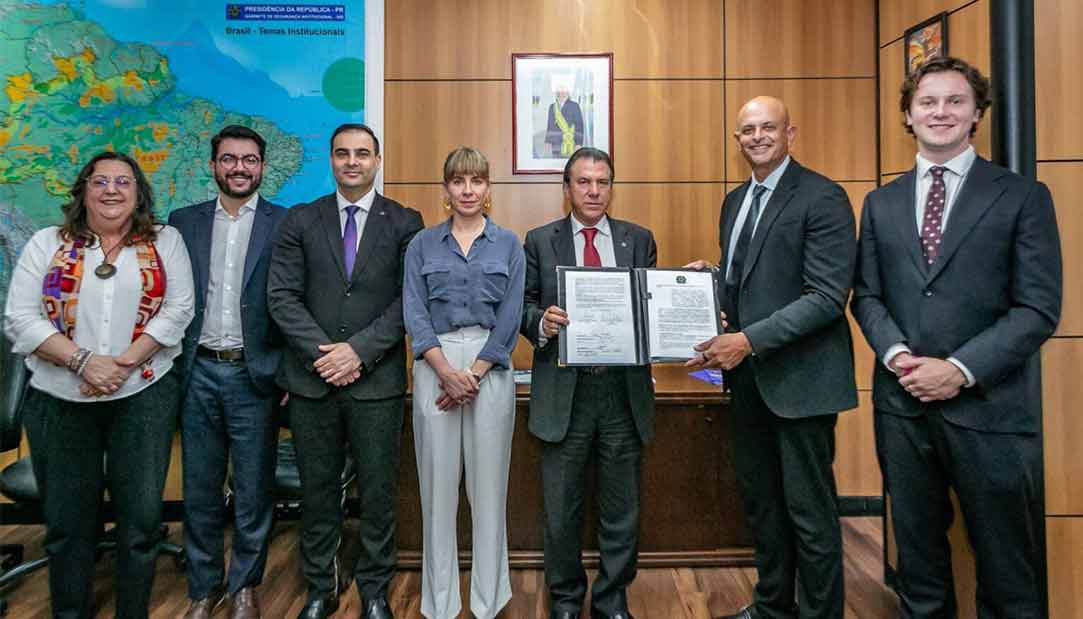 Grupo de autoridades e representantes em ambiente institucional, apresentando um documento oficial assinado durante um encontro formal