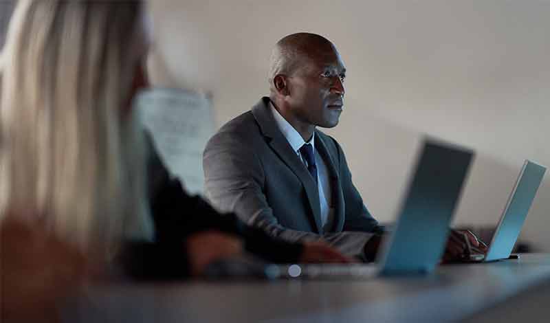 Profissionais colaborando em reunião corporativa com laptops.