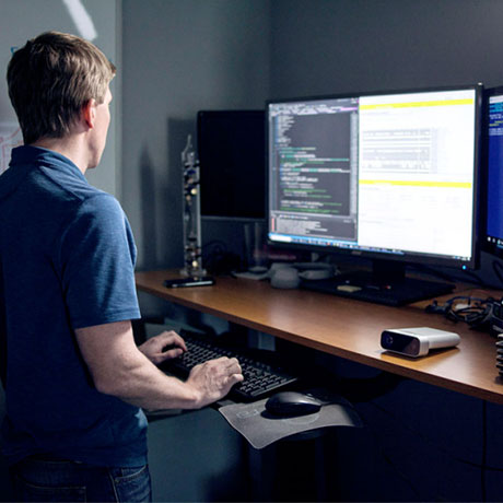 Homem em pé em frente a um computador analisa linhas de código