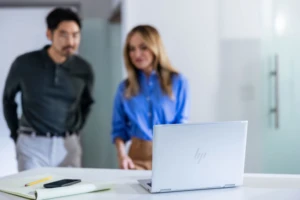 A laptop on a table with a man and woman in the background