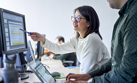 Image of a worker pointing something out to a coworker on her computer screen.