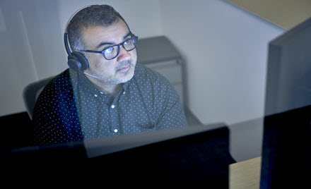 Image of a tech worker wearing headphones, looking at his computer screen.