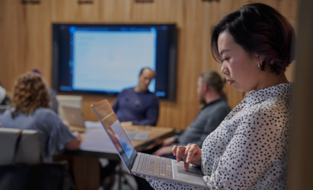 Women looking at Surface laptop with background of a conference room.