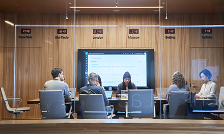 An image of a conference room or board room meeting including people sitting around table in a room with international time clocks.