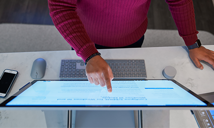 Top down view of a man wearing a dark red shirt working on a Microsoft Surface Studio.