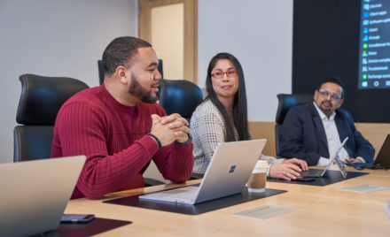 Group of people at a conference table with laptops who appear to be have a healthy and positive discussion or meeting.