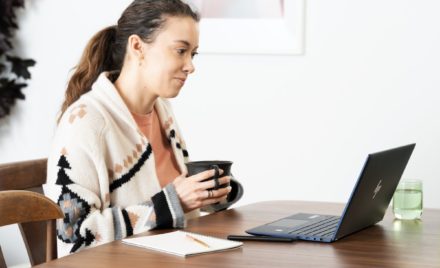 Woman holding a mug with laptop on dining room table with an HP Elite Dragonfly
