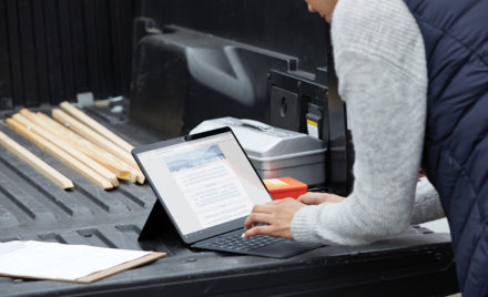 Adult female standing at the back of a pickup truck using a black Microsoft Surface Pro X in laptop mode with Microsoft Edge screen shown.