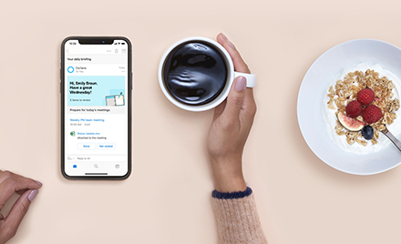 Image for: Cortana Daily Briefings on a mobile device. User holds a cup of coffee. Next to the coffee is a breakfast dish.