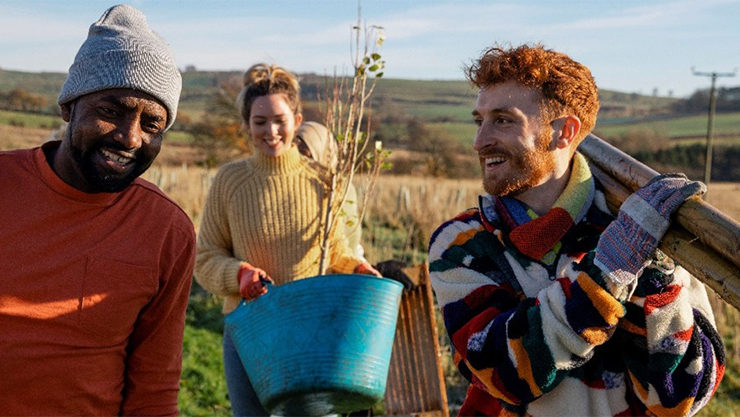 three people smiling and carrying objects in a field