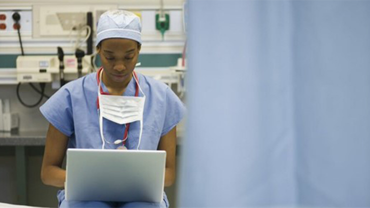 A nurse sitting down in the hospital while having a laptop in her lap