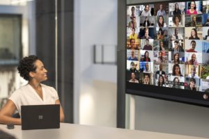 Adult female meeting in a conference room while using Microsoft Teams Together Mode on a Surface Hub 2S 85” device.